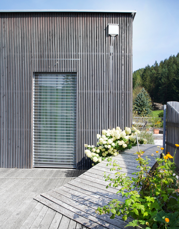 Atriumhaus Steg Holzfassade in elegantem silbergrau, Holzterrasse mit Steg, Zaun und Pflanzbehälter
